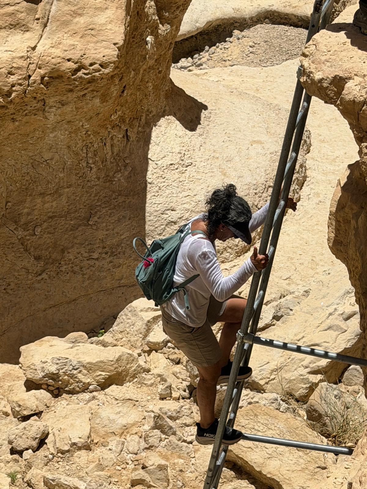 מטיילת עם תיק גב עולה בסולם מתכת בין סלעי קניון